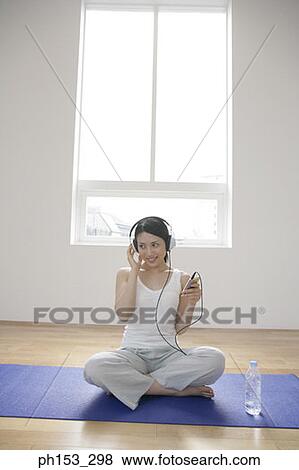 Stock Photo - Young woman sitting on an exercise mat and listening to music. Fotosearch