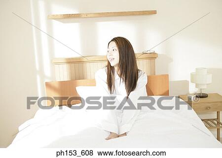 Young woman sitting on the bed View Large Photo Image Stock Photo - Young woman sitting on the bed. Fotosearch