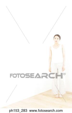 Stock Image - Young woman standing at the corner of a room. Fotosearch