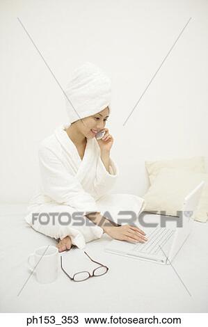 Young woman using a laptop and talking on a mobile phone on the bed View Large Photo Image Stock Image - Young woman using a laptop and talking on a mobile phone on the bed. Fotosearch