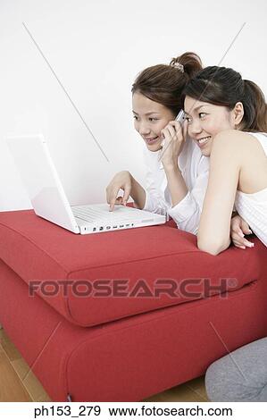 Young woman using a laptop and talking on a mobile phone with a young woman listening to her View Large Photo Image Stock Photo - Young woman using a laptop and talking on a mobile phone with a young woman listening to her. Fotosearch