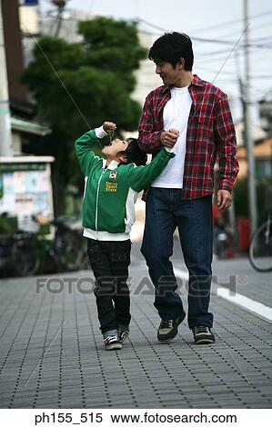 Stock Photography - Boy eating candy with his father walking behind him. Fotosearch