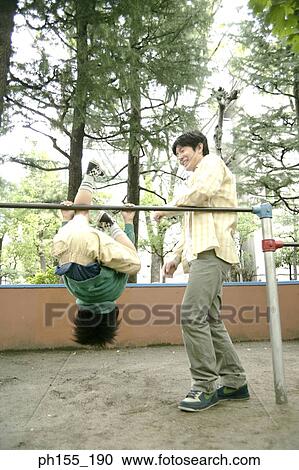 Boy hanging on monkey bars with his father standing beside him View Large Photo Image Stock Image - Boy hanging on monkey bars with his father standing beside him. Fotosearch