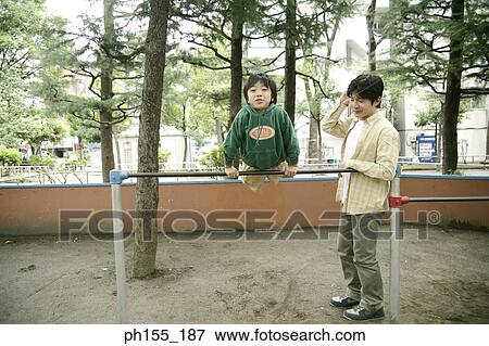 Stock Photo - Boy hanging on monkey bars with his father standing beside him. Fotosearch
