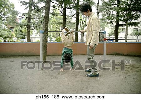 Boy hanging on monkey bars with his father standing beside him View Large Photo Image Stock Photography - Boy hanging on monkey bars with his father standing beside him. Fotosearch