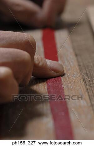 Stock Photo - Close-up of a person's fingers pasting ribbon around cardboard. Fotosearch