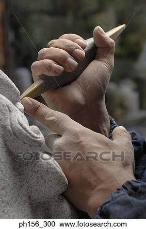 Stock Image - Close-up of a person's hand carving a statue with a chisel. Fotosearch