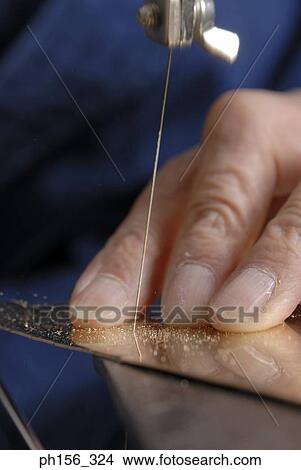 Picture - Close-up of a person's hand cutting a metal sheet with a hacksaw blade. Fotosearch