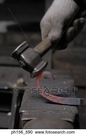 Stock Image - Close-up of a person's hand hitting a molten rod with a hammer. Fotosearch