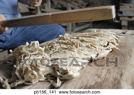 Stock Image - Close-up of a person's hand hitting animal hide with a wooden stick. Fotosearch