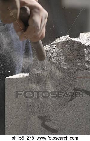 Stock Photo - Close-up of a person's hand using a chisel and a hammer on stone. Fotosearch