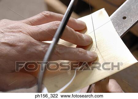 Stock Image - Close-up of a person's hands cutting metal sheet with a hacksaw blade. Fotosearch