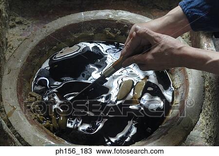 Stock Image - Close-up of a person's hands stirring wax in a container. Fotosearch