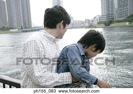 Stock Image - Close-up of a young man and his son looking down at water. Fotosearch