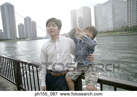 Stock Photo - Close-up of a young man and his son sitting on a railing. Fotosearch