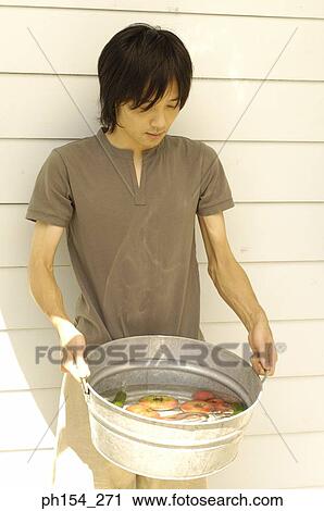 Stock Image - Close-up of a young man holding a washtub with vegetables. Fotosearch