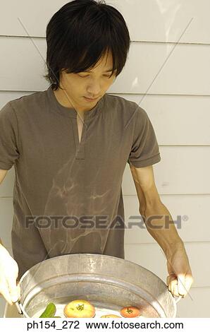 Stock Image - Close-up of a young man holding a washtub with vegetables. Fotosearch