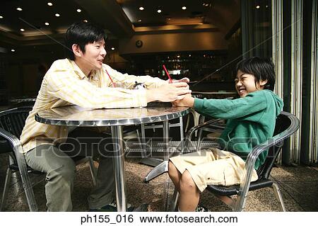 Stock Photograph - Close-up of a young man pulling a glass from his son in a restaurant. Fotosearch