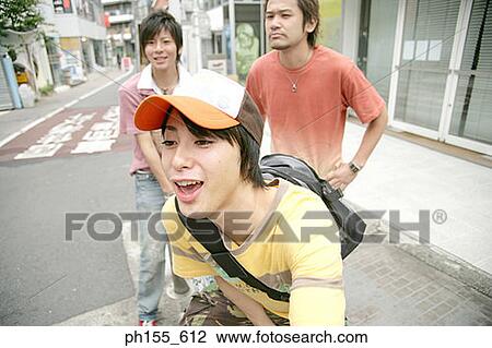 Close-up of a young man smiling with two young men standing behind him View Large Photo Image Stock Image - Close-up of a young man smiling with two young men standing behind him. Fotosearch