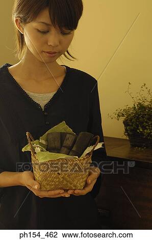 Stock Image - Close-up of a young woman holding a wicker basket with pieces of bamboo. Fotosearch