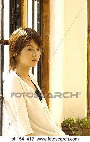 Close-up of a young woman leaning against a window and looking away View Large Photo Image Stock Photo - Close-up of a young woman leaning against a window and looking away. Fotosearch