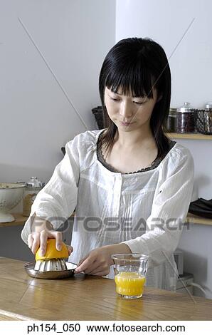 Stock Image - Close-up of a young woman squeezing an orange on a juicer. Fotosearch