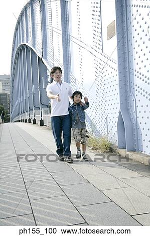 Stock Image - Father and his son walking on a bridge. Fotosearch