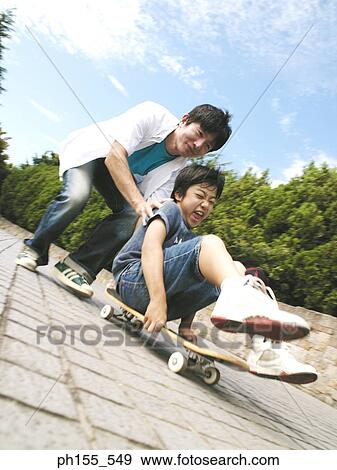Father pushing his son on a skateboard View Large Photo Image Stock Photo - Father pushing his son on a skateboard. Fotosearch
