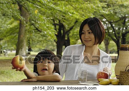 Stock Image - Girl holding an apple beside her mother. Fotosearch