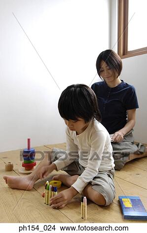 Picture - Girl playing with felt tip pens with her mother sitting behind her. Fotosearch