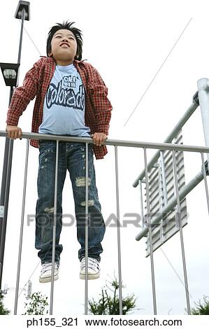 Stock Image - Low angle view of a boy leaning against a railing. Fotosearch