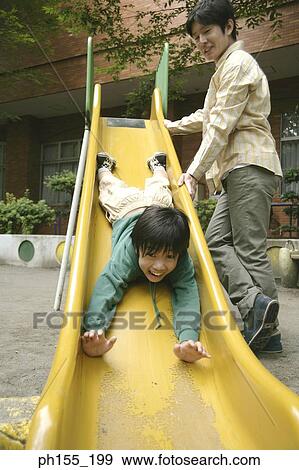 Low angle view of a boy sliding on a slide with his father standing beside him View Large Photo Image Stock Photo - Low angle view of a boy sliding on a slide with his father standing beside him. Fotosearch