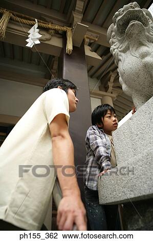 Stock Image - Low angle view of a mid adult man and his son standing near a statue of a lion. Fotosearch