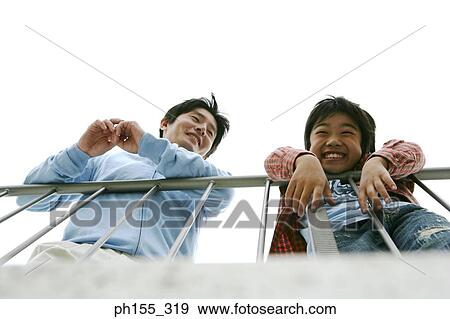 Stock Photo - Low angle view of a mid adult man and his son leaning against a railing. Fotosearch