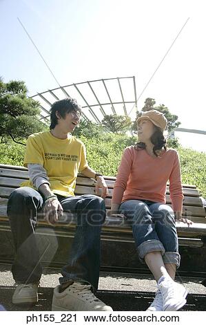 Low angle view of a young couple sitting on a park bench and smiling View Large Photo Image Stock Image - Low angle view of a young couple sitting on a park bench and smiling. Fotosearch