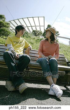 Low angle view of a young couple sitting on a park bench View Large Photo Image Stock Image - Low angle view of a young couple sitting on a park bench. Fotosearch