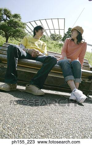 Low angle view of a young couple sitting on a park bench View Large Photo Image Stock Image - Low angle view of a young couple sitting on a park bench. Fotosearch