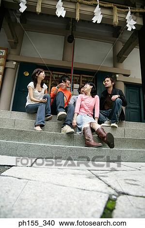 Low angle view of three young men and two young women sitting on steps and talking View Large Photo Image Stock Image - Low angle view of three young men and two young women sitting on steps and talking. Fotosearch