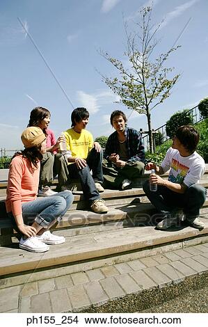 Low angle view of three young men with two young women sitting on steps and smiling View Large Photo Image Picture - Low angle view of three young men with two young women sitting on steps and smiling. Fotosearch