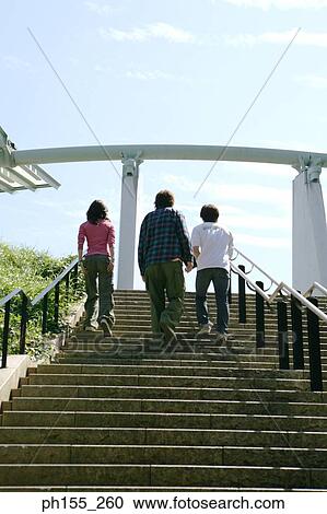 Stock Image - Low angle view of two men and a woman walking up steps. Fotosearch
