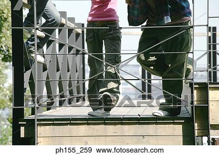 Stock Photo - Low angle view of two men and a woman on a footbridge. Fotosearch