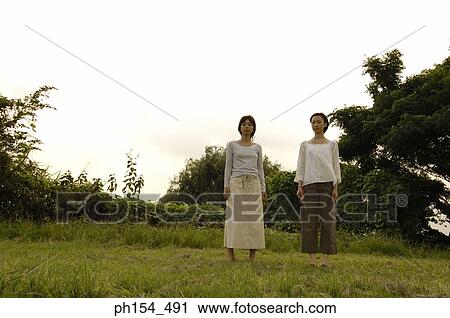 Stock Image - Low angle view of two young women standing in a field. Fotosearch