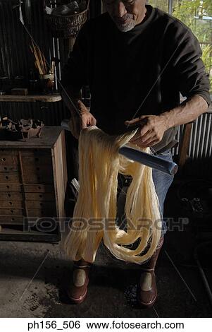 Stock Photograph - Mature man arranging silk threads on a wooden stick. Fotosearch