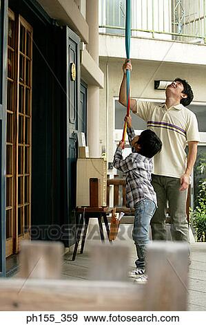 Stock Photo - Mid adult man and his son ringing a bell at a monastery. Fotosearch