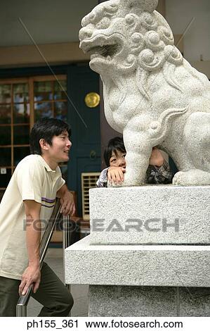 Mid adult man and his son standing near the statue of a lion View Large Photo Image Stock Image - Mid adult man and his son standing near the statue of a lion. Fotosearch