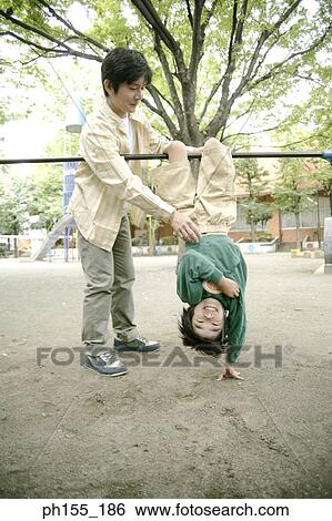 Stock Photograph - Mid adult man helping his son on monkey bars. Fotosearch