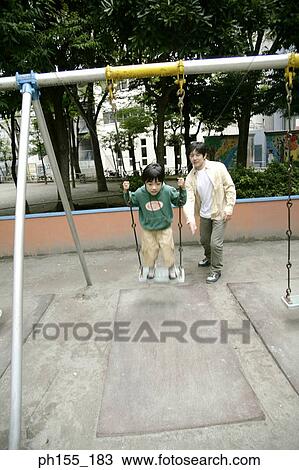 Stock Image - Mid adult man pushing his son on a swing. Fotosearch