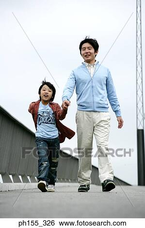 Stock Photograph - Mid adult man walking on the road and holding his son's hand. Fotosearch