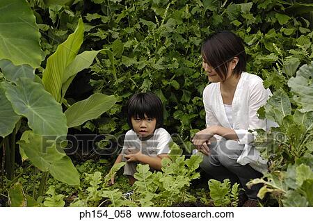 Stock Photo - Mid adult woman and her daughter crouching in a garden. Fotosearch