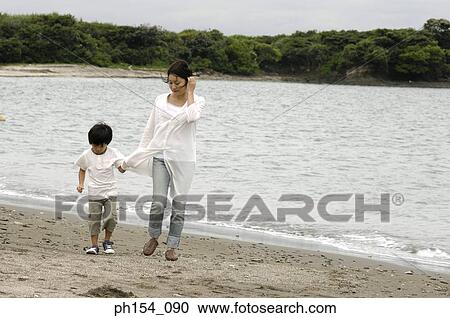 Stock Image - Mid adult woman walking with her son on the beach. Fotosearch